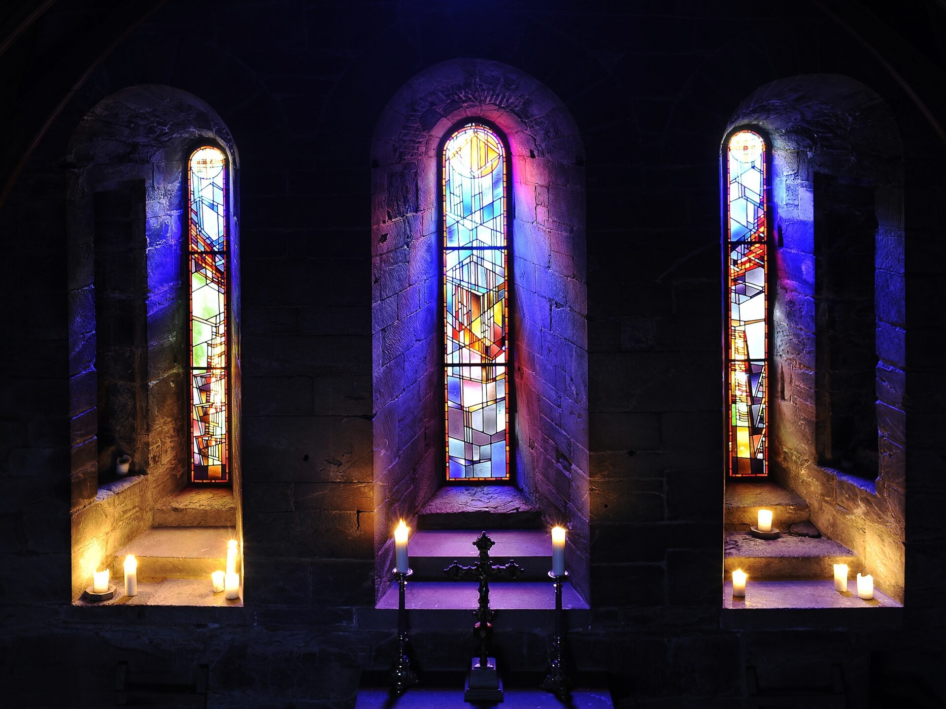 Tre fargerike blyglassvinduer i et mørkt kapell. Tre fargerike blyglassvinduer i et mørkt kapell.