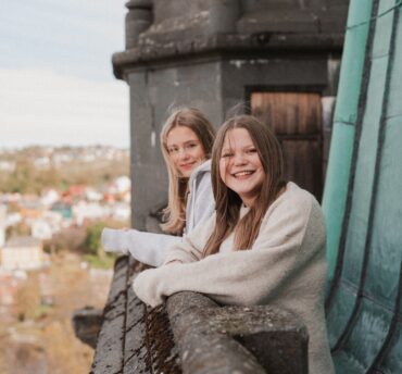 To unge jenter står og smiler og ser på utsikten fra tårnet i Nidarosdomen.
