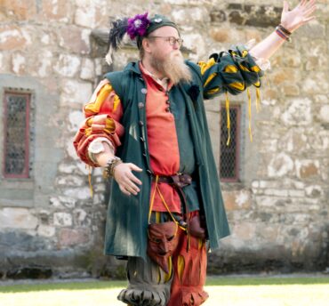 En mann utkledd som gjøgler løfter hånden og vinker.