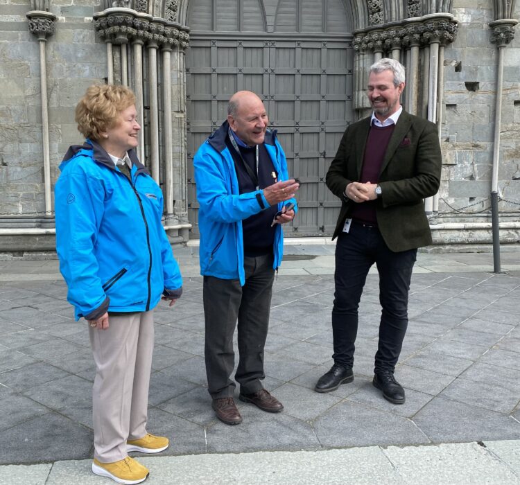 Et eldre par står utenfor Nidarosdomen og snakker med en mann i dress.